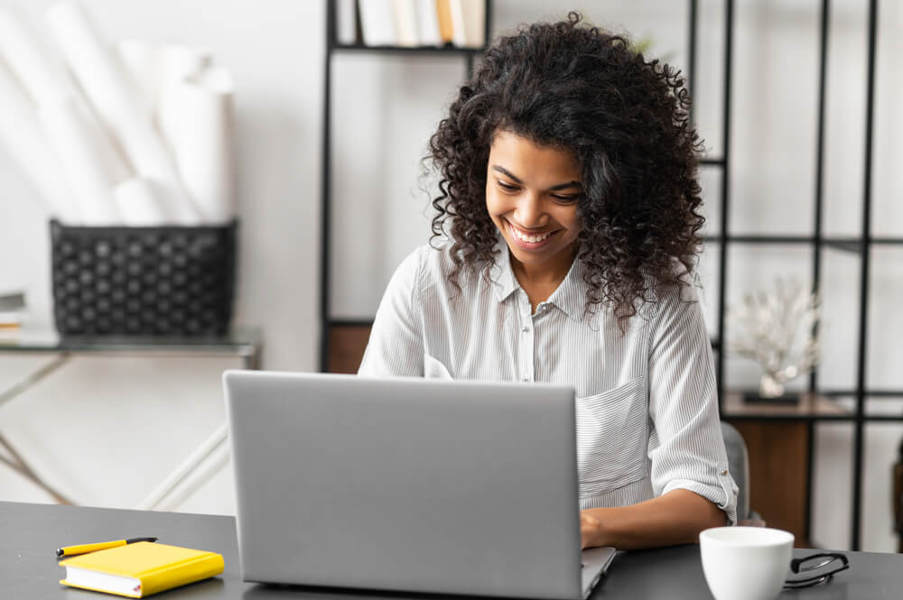 Portrait of a Young African American Woman Sitting at the Desk With a Laptop, Typing an Email