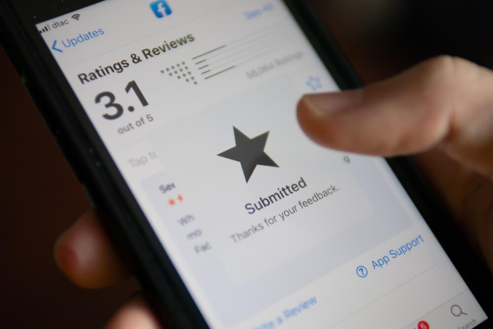 Phone User Tap on a Star to Rate the Facebook App on App Store.